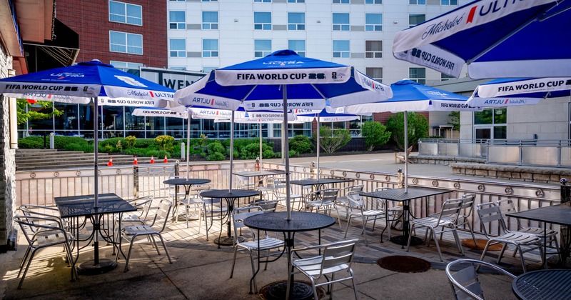 Outdoor seating area with metal tables and chairs, shaded by branded umbrellas