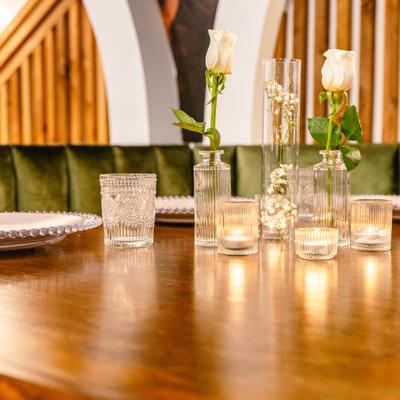 Table setting featuring white roses in glass vases, small candles, plates and glasses.