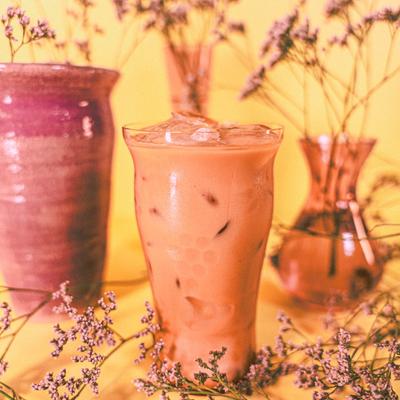 Iced chai latte with floral decor and colorful vases on a yellow background.