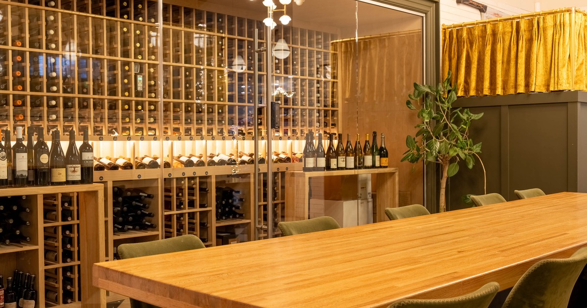 Wine cellar with a wooden table and chairs, glass wall, wine bottles in racks and a potted plant