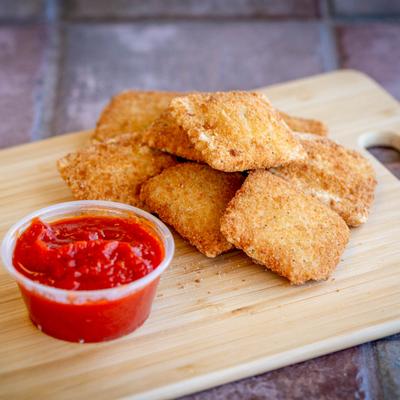 A wooden board holds fried ravioli with a side of marinara  sauce.