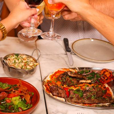 A group of patrons clink glasses in a toast over a table with served meals.