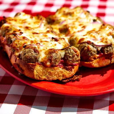 Cheesy meatball sub on red plate, close up.