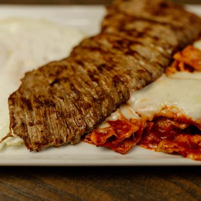 Close-up of a carne asada steak served with fried eggs and chilaquiles.