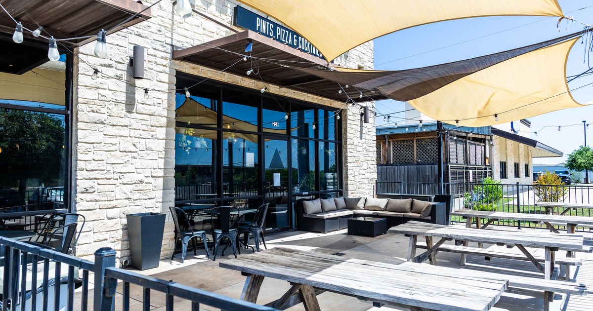 Exterior seating area with picnic tables beneath triangle shade sails