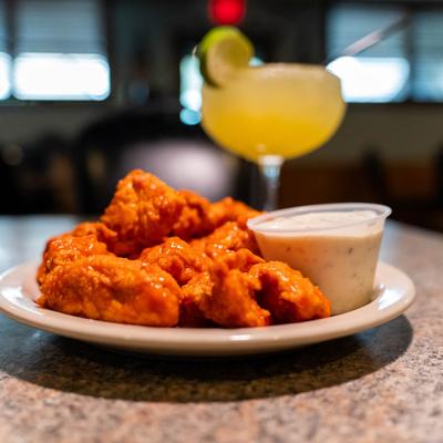 Buffalo chicken tenders with ranch dip and a margaraita in the background.