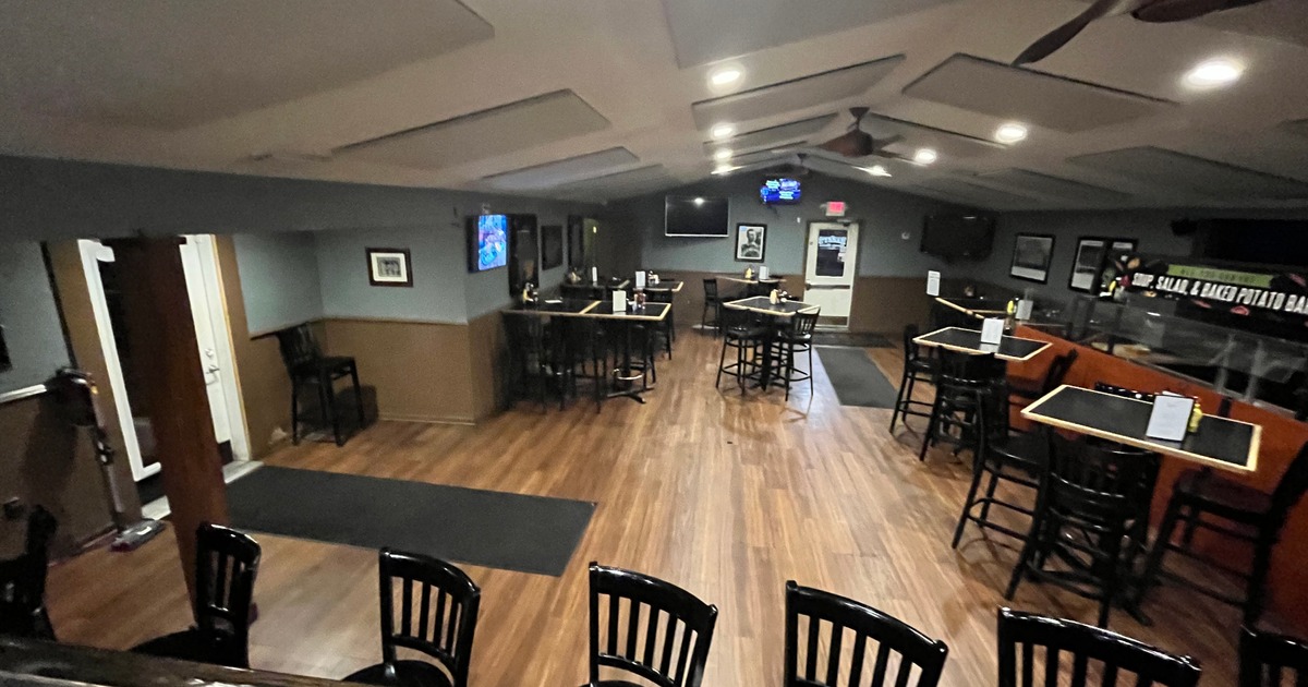 Interior, features wood flooring, high-top tables with black chairs, and ambient lightin