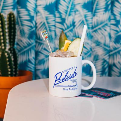 White mug holds a tropical drink garnished with fruit and a straw on a table.
