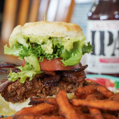 Fried chicken biscuit sandwich with bacon, tomato, and  lettuce, served with sweet potato fries.