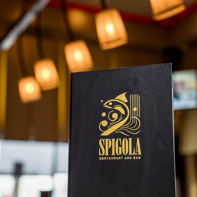 Black menu of Spigola Restaurant and Bar featuring a gold fish logo.