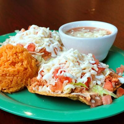 Chicken tostada served with Mexican rice, salad, and refried beans.