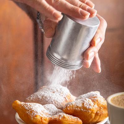 Dusting beignets with powdered sugar.