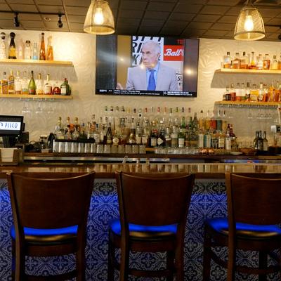 A dimly lit modern restaurant bar features patterned blue tiles and wooden chairs.