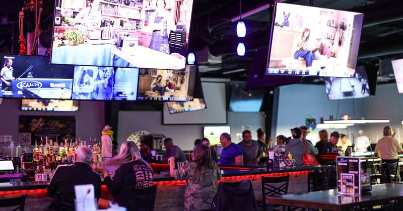 The interior of a lively sports bar, featuring multiple large-screen TVs, patrons on bar area