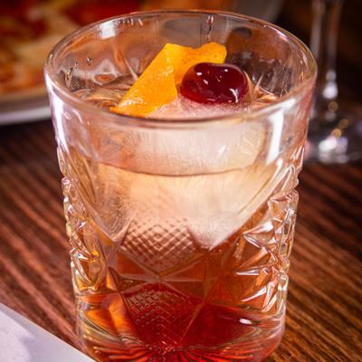 Old fashioned cocktail in a whisky glass with an orange peel and a cherry.