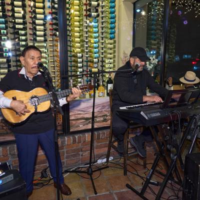 Musicians performing  in front of a wine rack.