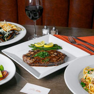 Grilled ribeye steak with green beans and lime slices, accompanied by red wine and mussels.