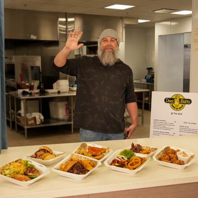 Chef waving behind counter with served portions of food.