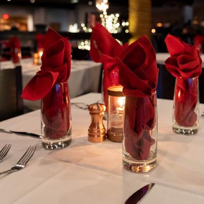 Elegant restaurant table setting with red napkins in glasses, a lit candle on a white tablecloth.