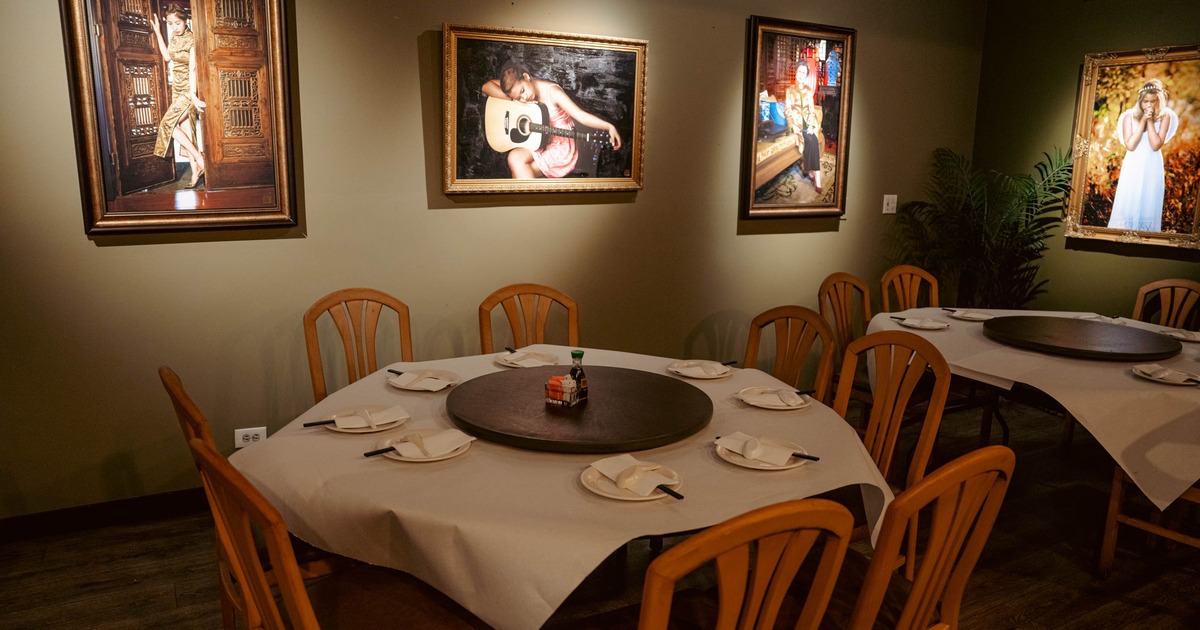 Restaurant interior with paintings on the wall and round dining tables below.