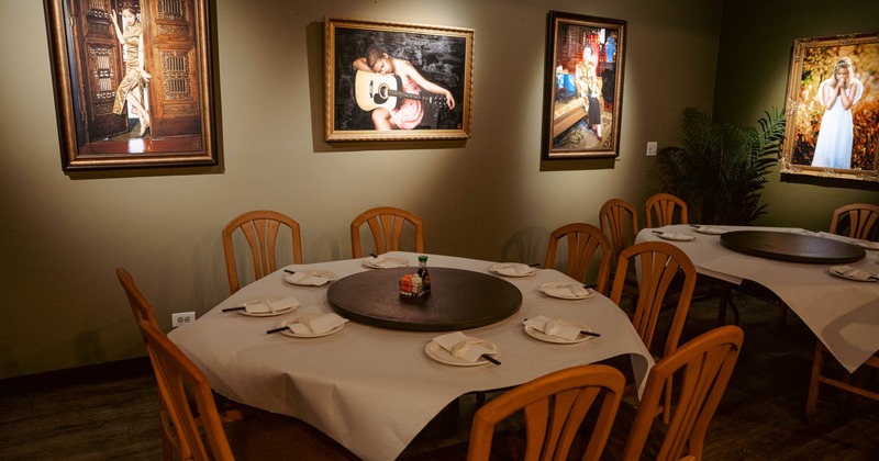 Restaurant interior with paintings on the wall and round dining tables below.