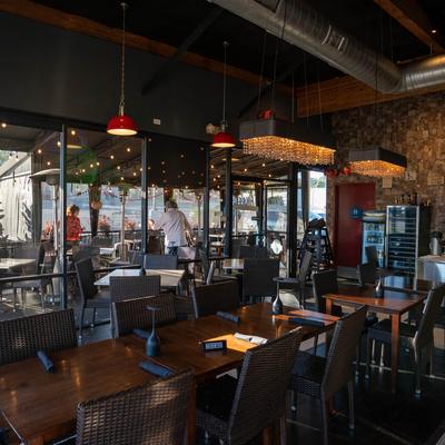 Modern restaurant interior with warm lighting, glass walls, wooden tables, and seating.