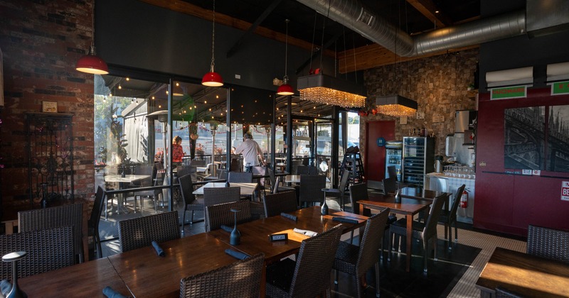 Interior of a cozy restaurant with wooden tables and chairs, red pendant lights, and large windows