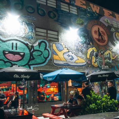 Colorful street mural above the outdoor restaurant seating with umbrellas.