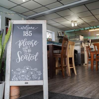A chalkboard sign reading 'Welcome to 185, Please wait to be seated'.