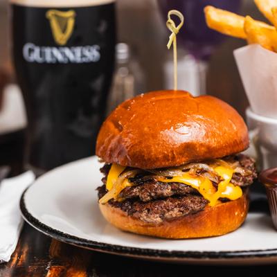 Double cheeseburger with melted cheese on a toasted brioche bun, served with fries and a dark beer.