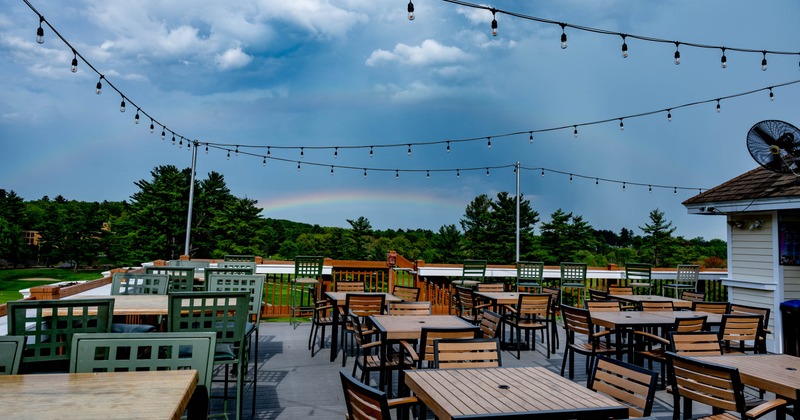 Outdoor patio area with wooden tables and chairs, strings of lights above