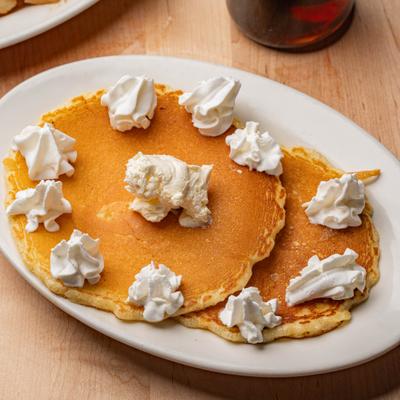 Pancakes topped with a dollop of butter and multiple swirls of whipped cream.