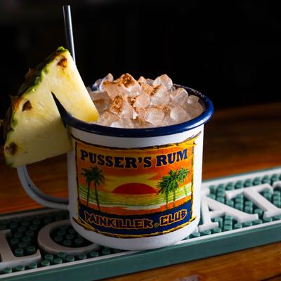 Painkiller cocktail served in painkiller club cup, garnished with pineapple wedge.