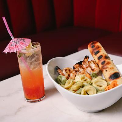 Tortellini pasta paired with grilled prawns and bread stick, alongside a cocktail.