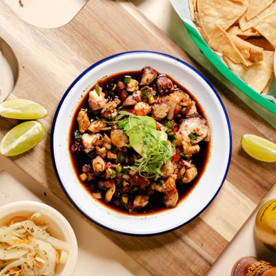 Seafood cocktail in tomato-based broth topped with avocado and microgreens.