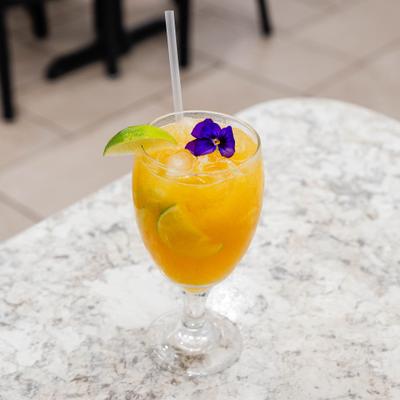 Orange drink garnished with lime and purple flower.