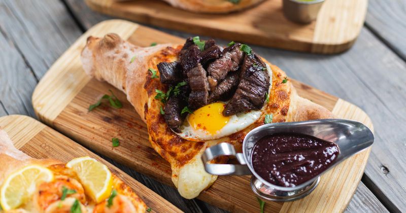 Steak and eggs cheese boat served with dark sauce on a wooden board