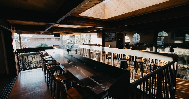 An interior view of a modern bar with a long marble counter and high stools
