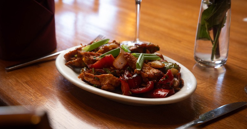 Stir-fried chicken with peppers and scallions accompanied by a glass of red winr