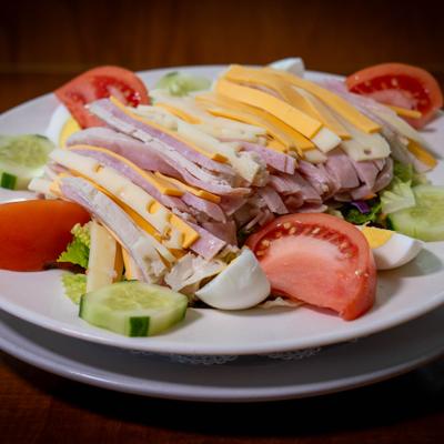 Salad with sliced ham, cheese, tomatoes, cucumber rounds,, boiled egg, and lettuce.