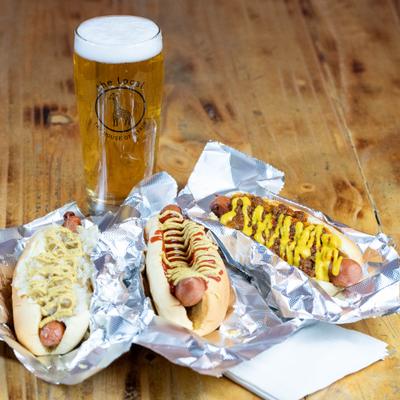 Assorted hot dogs served on foil paper with a glass of light beer.