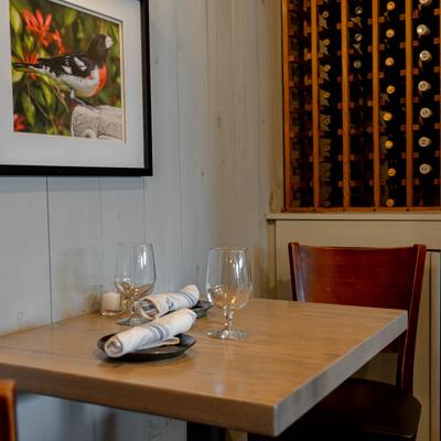 Corner table set for two beside a wine rack and a bird photo on a wall.