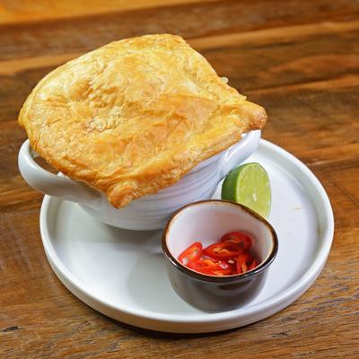 Onion soup topped with flaky pastry, served with lime and chili slices.