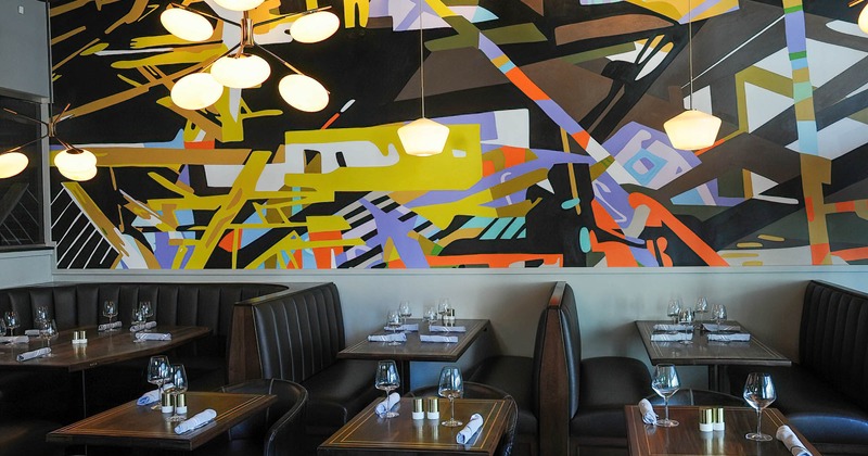 Interior, lined up tables and seating, large contemporary mural on the wall