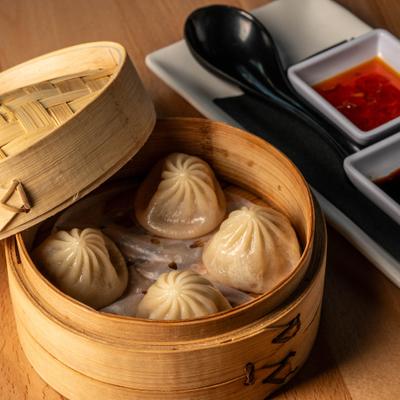 Soup Dumplings served in small bamboo baskets with sauces on the side.