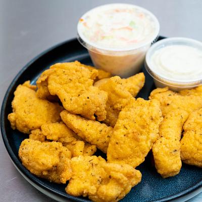 Catfish nuggets served on a dark blue plate with tartar sauce and coleslaw.