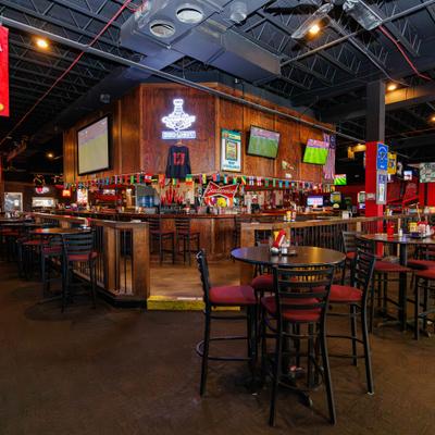 Spacious sports bar features wooden decor, multiple televisions, tables, and team banners.
