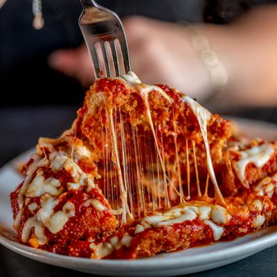 Chicken parmesan on a white plate with melted cheese being lifted by a fork.
