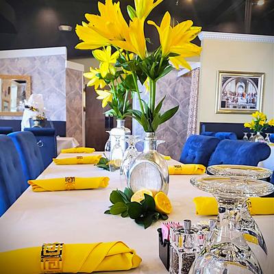 Dining setup with yellow flowers in glass vases and yellow napkins on a white table.