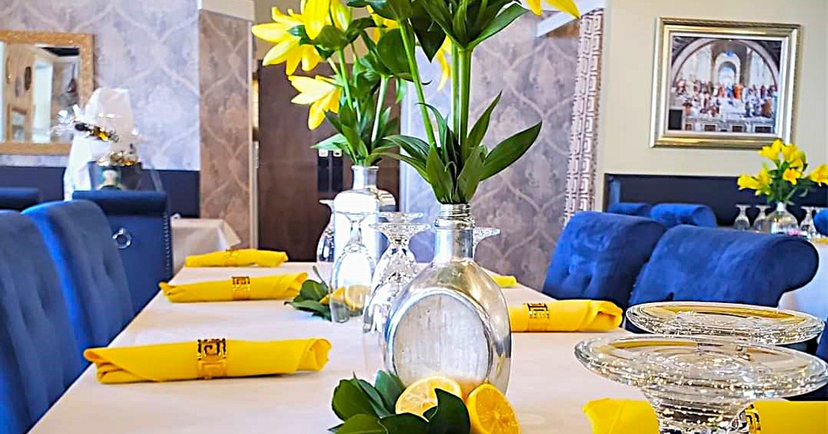 Elegant dining setup with a white tablecloth, yellow napkins, yellow flowers,  and blue chairs
